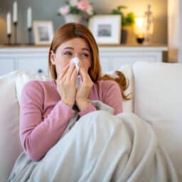 Sick woman blowing nose while sitting on sofa at home