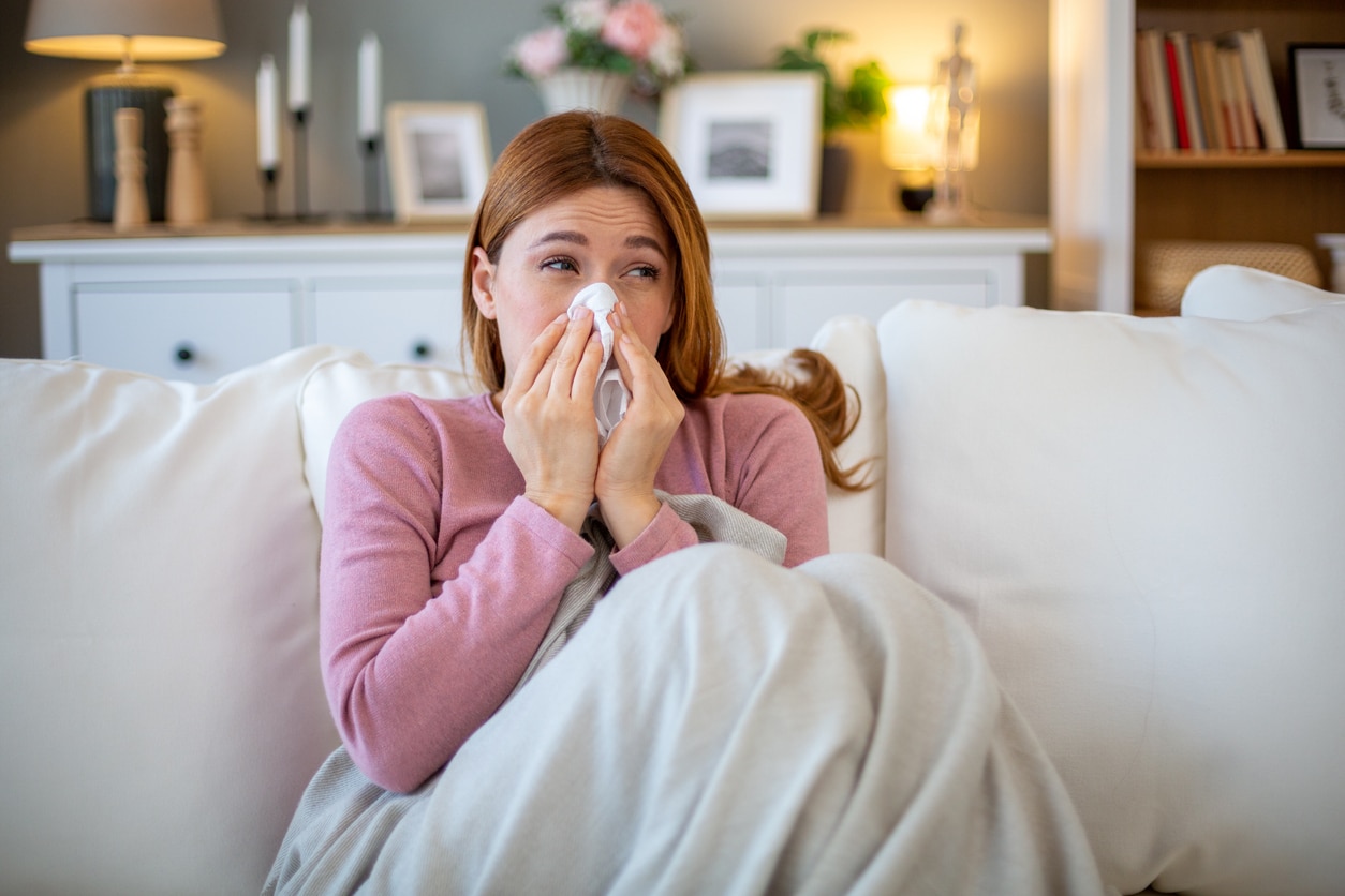 Sick woman blowing nose while sitting on sofa at home.