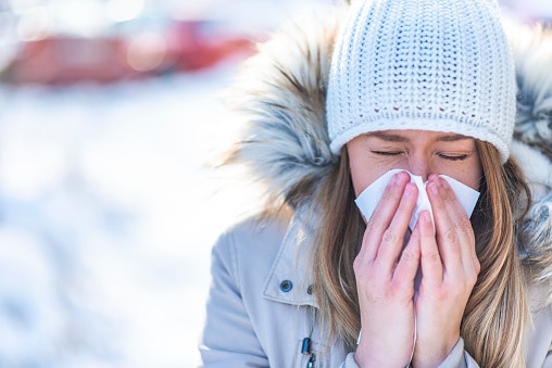 Woman blowing in a tissue in a cold winter with a snowy mountain in the background.