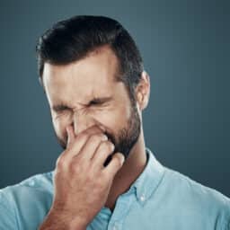 Man covering nose with hand while standing against grey background.