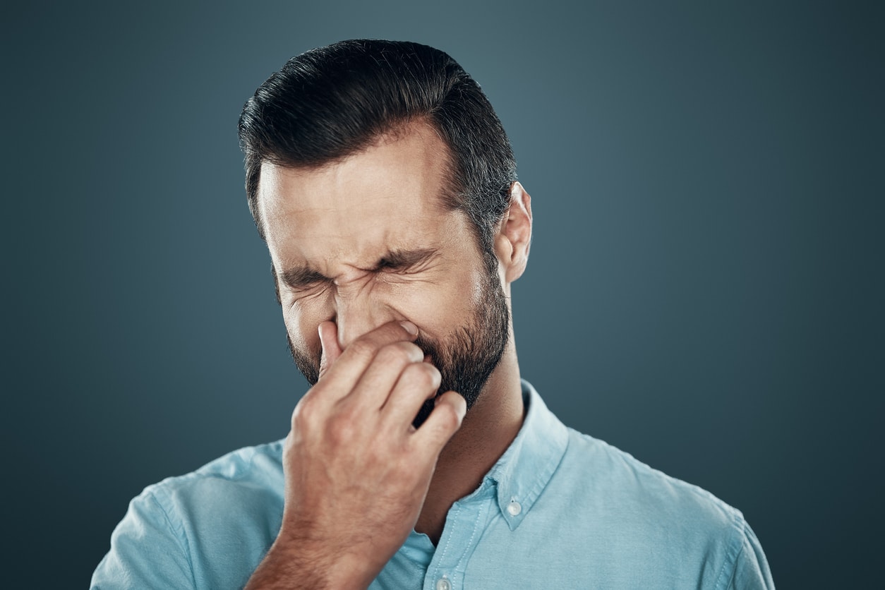 Man covering nose with hand while standing against grey background.