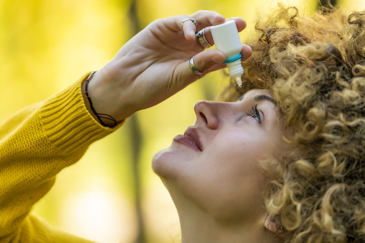 Young woman putting eye drops in her eyes.