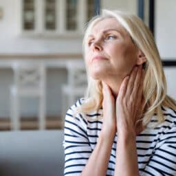 Senior woman with postnasal drip holding her throat.