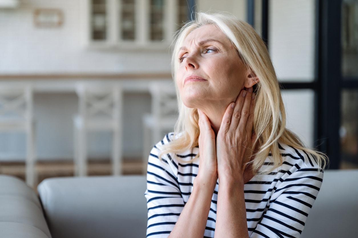 Senior woman with postnasal drip holding her throat.