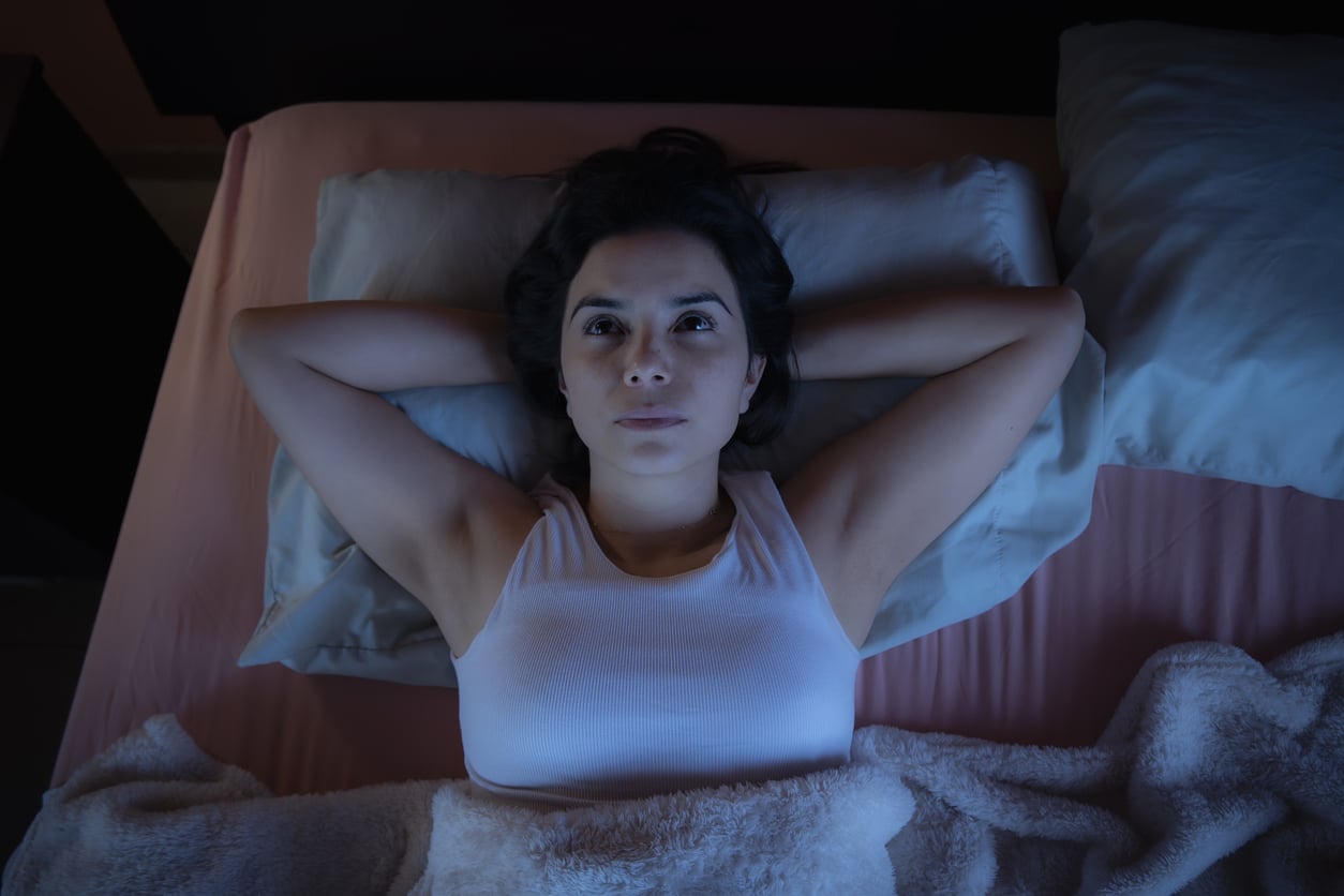 Woman lying awake in bed at night staring at ceiling.
