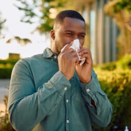 Man with allergies blowing his now outdoors