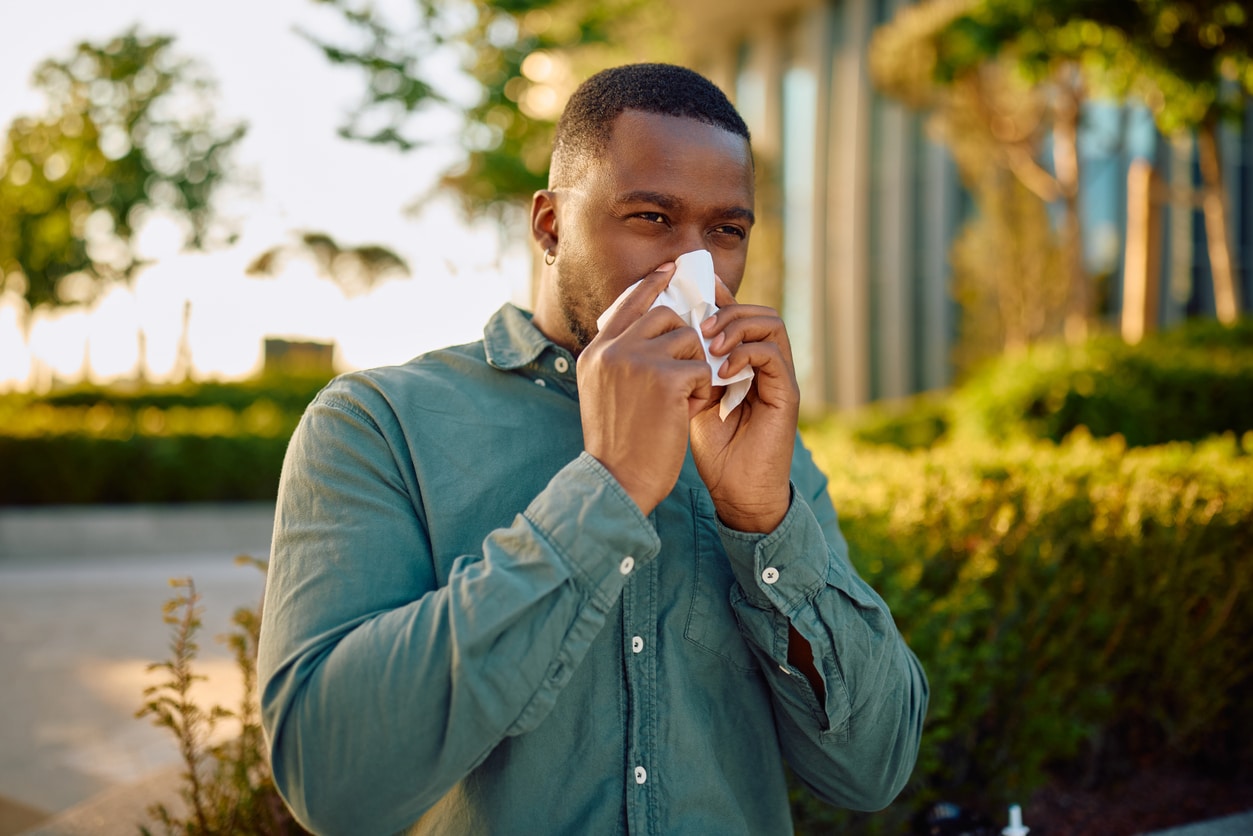 Man with allergies blowing his now outdoors.