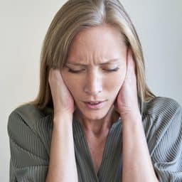 Close-up of young woman with eyes closed covering her ears.