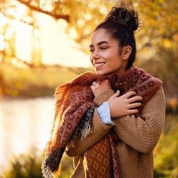 Smiling woman bundled up in a sweater and scarf in the park.