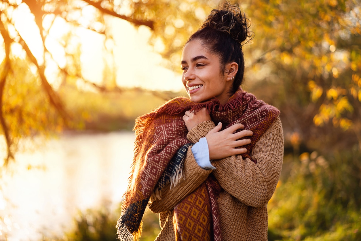 Smiling woman bundled up in a sweater and scarf in the park.