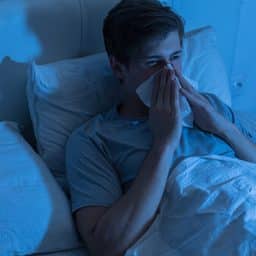 Young man lying in bed and blowing his nose.