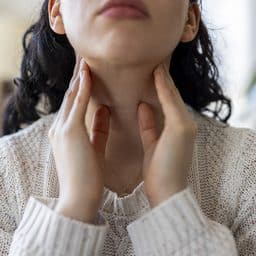 A close-up shot of a young woman touching her neck and throat with her fingers.