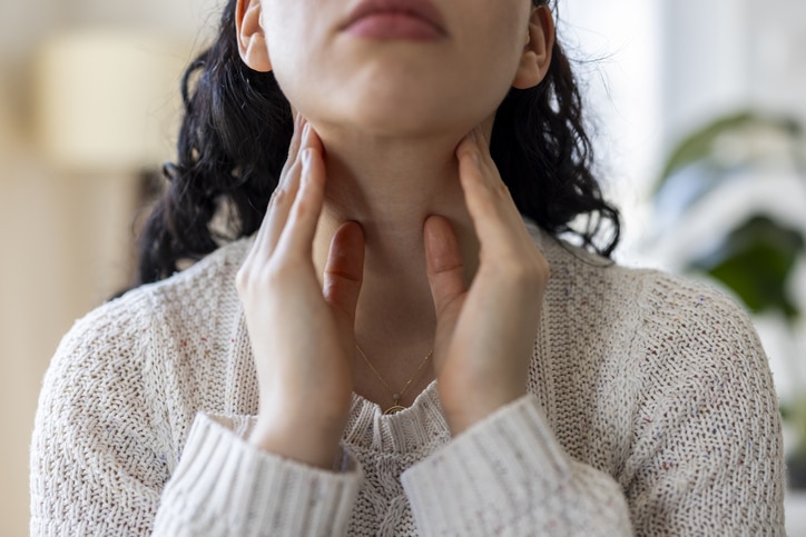 A close-up shot of a young woman touching her neck and throat with her fingers.